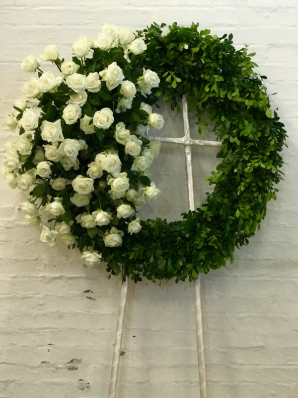 Suspiro, corona fúnebre con rosas blancas y follaje. Condolencias para envíos a Monterrey y San Pedro. 